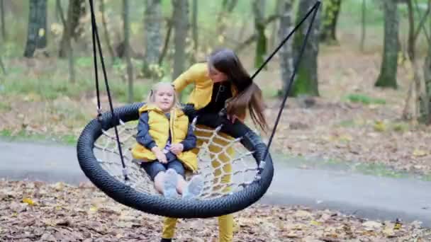 Mam en dochter hebben plezier samen. jong vrouw en klein meisje swing op een swing in de herfst park — Stockvideo