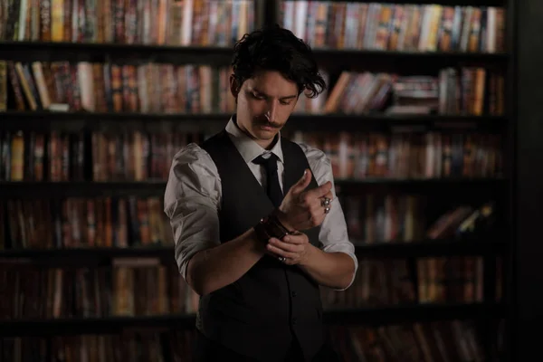 pensive man stands at night in a dark library room. stylish man with a mustache straightens the bracelet.