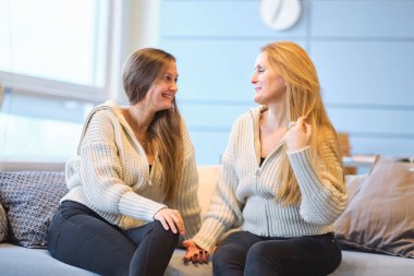 Mutlu anne ve arkadaş canlısı kız el ele tutuşup birbirlerine bakıyorlar. Anne yetişkin kız kanepede oturmuş gülümsüyor. Sarılmak mutlu hissettiriyor. Birlikte vakit geçirmek. Sevgi kavramı.