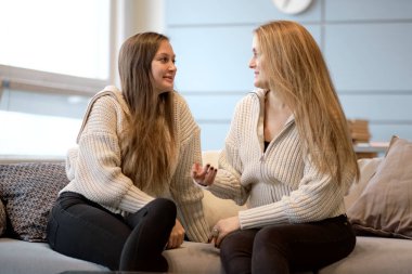 Mutlu anne ve arkadaş canlısı kız el ele tutuşup birbirlerine bakıyorlar. Anne yetişkin kız kanepede oturmuş gülümsüyor. Sarılmak mutlu hissettiriyor. Birlikte vakit geçirmek. Sevgi kavramı.