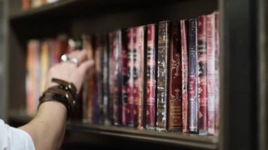 Şık giyimli bir adam eski karanlık bir kütüphanede klasik bir kitap seçiyor. Manzarayı kapat. Manzarayı kapat. Yavaş çekim nvideo.