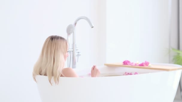 Frumos Sexy Caucazian Blonda Fata În Bikini Lying În Flower Bath În Resort Day Spa Salon. Terapia de îngrijire a pielii. Conceptul de femeie tânără relaxare în tubul de baie. Slow motion video. imagini din stoc — Videoclip de stoc