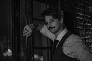 Şık giyinmiş bir adam pencerede durur ve mesafeye bakar. Düşünceli adam gece karanlık bir odada duruyor.