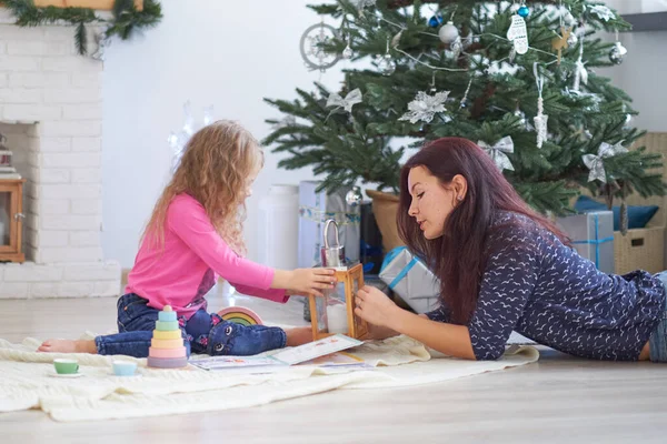 Positif mignon jeune femme maman s'assoit sur le sol dans un studio festif et joue avec la petite fille.. — Photo