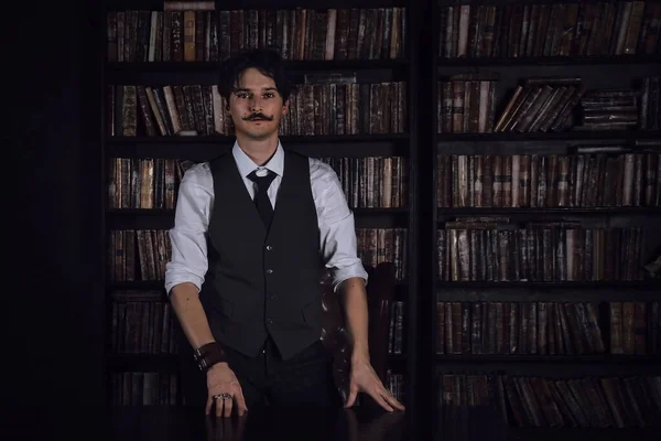 pensive man stands at night in a dark library room. stylish man with a mustache straightens the bracelet.