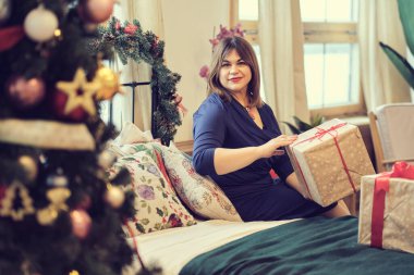 Noel ağacının yanındaki kadın tefekkür ediyordu. Annem hediyeler hazırlar, orta yaşlı kadın evdeki oturma odasında hediyelerle kutuları düzenler. yumuşak odak, sıcak tonlarda