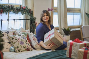 Noel ağacının yanındaki kadın tefekkür ediyordu. Annem hediyeler hazırlar, orta yaşlı kadın evdeki oturma odasında hediyelerle kutuları düzenler. Yumuşak odaklanma, sıcak tonlar. yumuşak odak