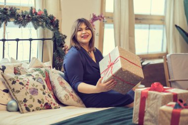 Noel ağacının yanındaki kadın tefekkür ediyordu. Annem hediyeler hazırlar, orta yaşlı kadın evdeki oturma odasında hediyelerle kutuları düzenler. Yumuşak odaklanma, sıcak tonlar. yumuşak odak