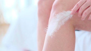 Tanımlanamayan bir kadın beyaz bir tüyü teninde gezdiriyor. Deri epilasyonu konsepti. Kışın cilt bakımı. görünümü kapat.