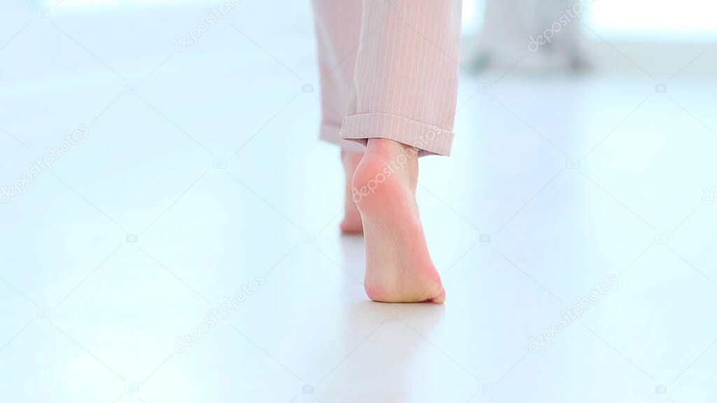 Side close up view of unrecognizable woman feet legs, barefoot girl standing indoors inside of modern home enjoy warm wooden heated floor. soft focus