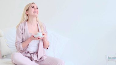 Romantik bir ortamda bir fincan kahveyle güzel genç bir kadın. Kahve fincanı olan kadın koltukta oturan kameraya bakıyor..