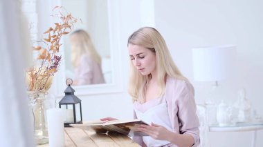 Genç ve güzel bir kadın oturma odasındaki masada bir kitap okuyor. yumuşak odak