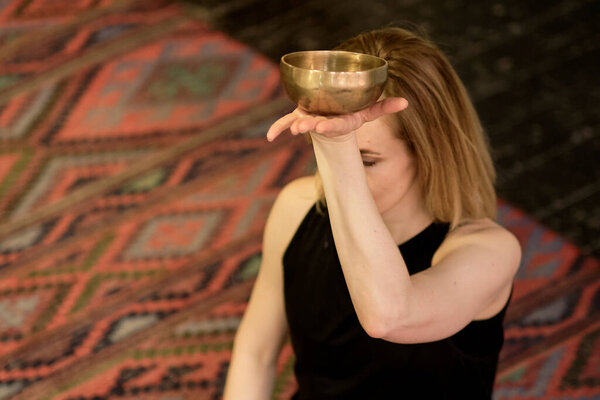 Женщина, играющая на тибетской поющей чаше, сидя на коврике для йоги. Винтажные тонны.