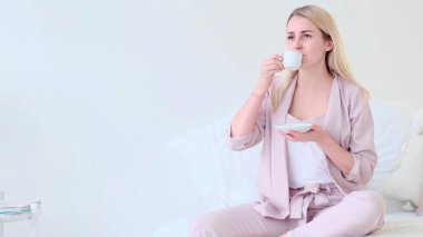 Romantik bir ortamda bir fincan kahveyle güzel genç bir kadın. Kahve fincanı olan kadın koltukta oturan kameraya bakıyor..