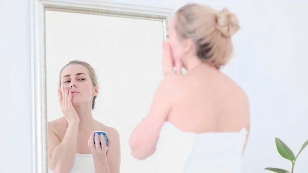 Güzel bir kadın sıcak banyodaki ayna yansımasına bakarken yüzüne krem sürüyor.. — Stok fotoğraf