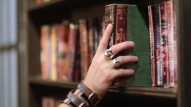 Şık giyimli bir adam eski karanlık bir kütüphanede klasik bir kitap seçiyor. Manzarayı kapat. Manzarayı kapat. Yavaş çekim nvideo.