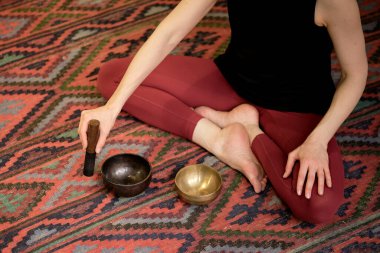 Kadın yoga minderinde otururken Tibet şarkı kasesinde oynuyor. Klasik tonlama.