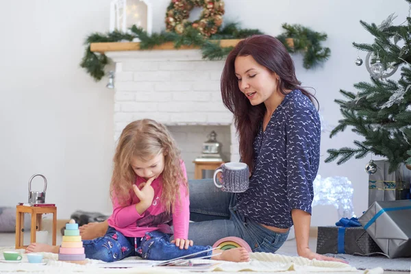 Positive cute young woman mom sits on floor in a festive studio and plays with little girl.. Good Christmas mood concept Stock Image