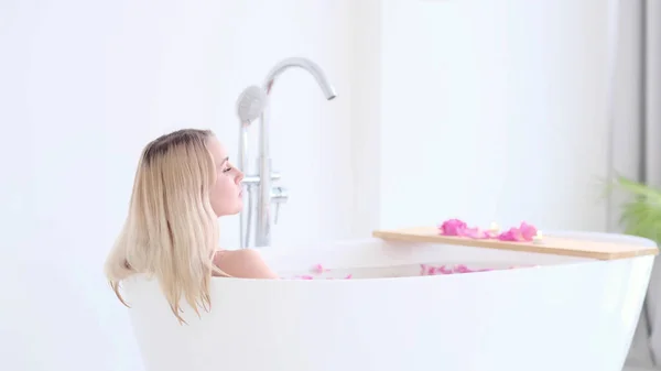 Linda menina loira caucasiana de biquíni deitado em banho de flores no Resort Day Spa Salon. Terapia de Cuidados com a pele. Conceito jovem mulher relaxante no tubo de banho. — Fotografia de Stock