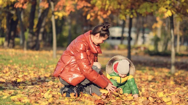 Mom and son throw autumn leaves in autumn park, family fun. family enjoying a walk in nature. happy motherhood concept. — Stock Photo, Image