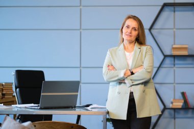 İnsanlar, yaş, teknoloji ve iş kavramı. İyi görünümlü orta yaşlı kadın yönetici ofiste kolları bağlı duruyor..