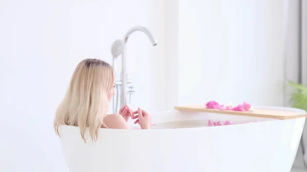 リゾート・デイ・スパ・サロンで花風呂に寝そべっているビキニの美しい白人ブロンドの女の子。スキンケア療法。コンセプト若いです女性リラックスでザバスチューブ. — ストック写真