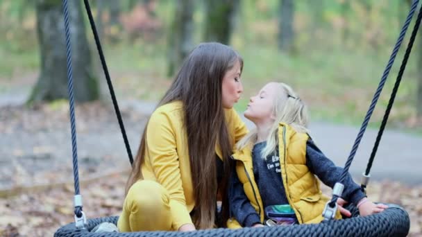 Mamá y su hija se divierten juntas. joven mujer y niña columpio en un columpio en el parque de otoño — Vídeos de Stock