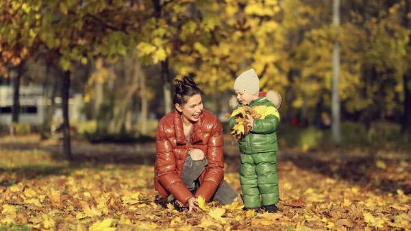 Mom and son throw autumn leaves in autumn park, family fun. family enjoying a walk in nature. happy motherhood concept. — Stock Photo, Image