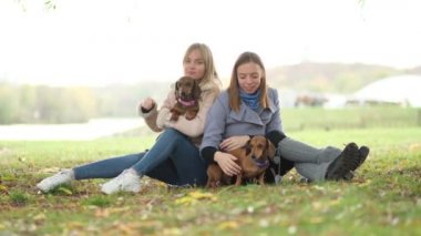 Ağır çekim. Parkta iki kız arkadaş köpekleriyle oynuyorlar. kız kardeş ilişkisi. Parkta oynayıp eğlenerek bir gün geçir. Görüntüyü kapat.