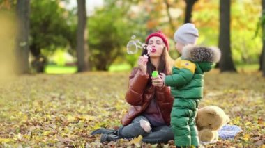 Genç anne ya da dadı parkta oynuyorlar. Annem sabun köpüğü üflüyor. Sonbaharda doğada yürümek. Mutlu bir aile. Manzarayı kapat. Yavaş çekim videosu. depolama görüntüleri