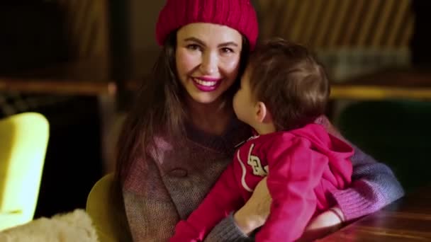 Веселая очаровательная молодая мама и милый маленький сын сидят вместе в кафе, обнимаются, улыбаются и веселятся вместе — стоковое видео