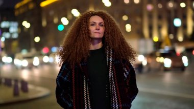 Güzel genç bir kadın kameraya bakıyor ve neşeyle gülümsüyor. Gün ışığında sokakta gülen surat. Dışarda olumlu bir portre.