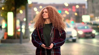 Güzel genç bir kadın kameraya bakıyor ve neşeyle gülümsüyor. Gün ışığında sokakta gülen surat. Dışarda olumlu bir portre.