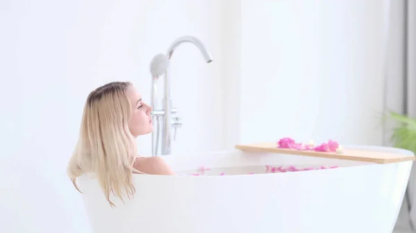 Hermosa chica rubia caucásica en bikini acostado en el baño de flores en Resort Day Spa Salon. Terapia de cuidado de la piel. Concepto de mujer joven relajándose en la bañera. — Foto de Stock