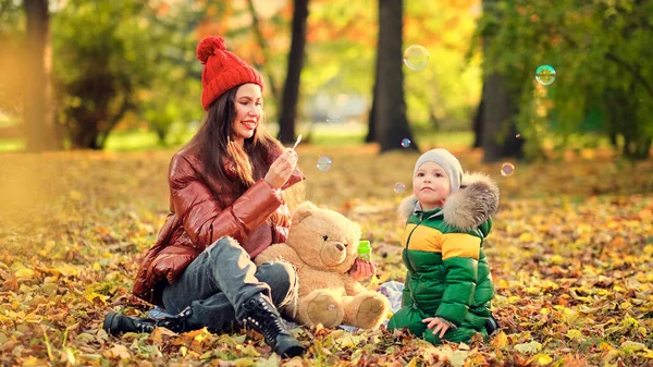 Adult mother or nanny blows bubbles for a little boy. happy motherhood. cute kid playing in the park. — Stock Photo, Image