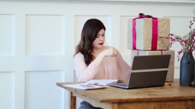 Masada oturan, dizüstü bilgisayarda yazan ve hediye kutularıyla konuşan güzel genç bir bayan. kutu evde iyi online alışveriş alır, posta sevkiyatı konsepti