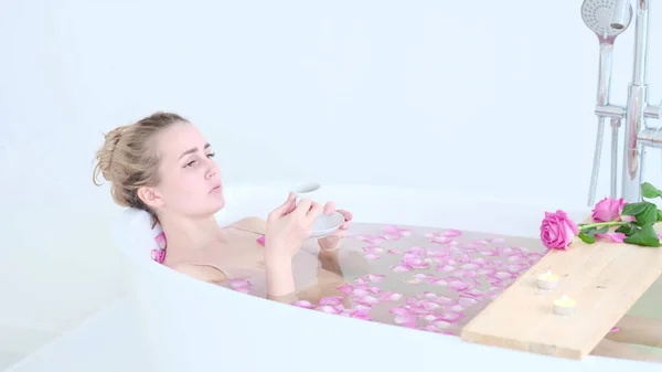 リゾート・デイ・スパ・サロンで花風呂に寝そべっているビキニの美しい白人ブロンドの女の子。スキンケア療法。コンセプト若いです女性リラックスでザバスチューブ. — ストック写真
