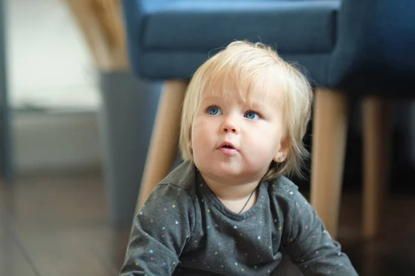 Retrato lindo de uma criança de 2 anos. Cabelo loiro, olhos azuis bebê olha para o lado na sala de estar — Fotografia de Stock