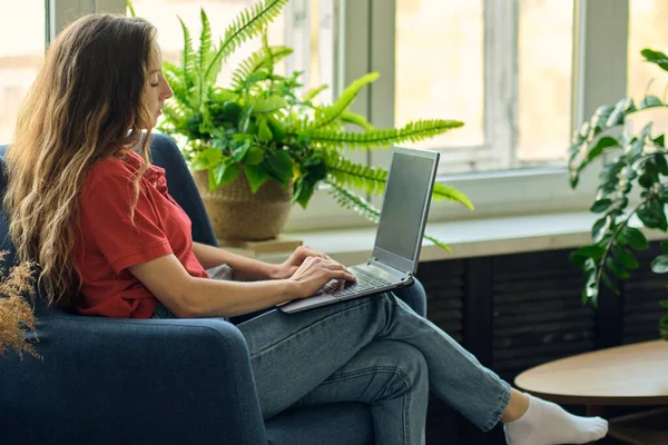 A fiatal nő laptopot használ munka után, kommunikál az interneten az ügyféllel. Boldog szabadúszó nő pihentető kényelmes kanapén, és a laptop otthon. — Stock Fotó