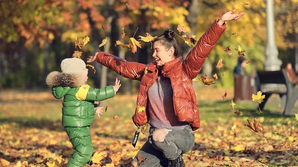 Mãe e filho jogam folhas de outono no parque de outono, diversão em família. família desfrutando de um passeio na natureza. conceito de maternidade feliz. — Fotografia de Stock