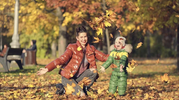 Mamma och son kastar höstlöv i höstparken, familjekul. familjen njuter av en promenad i naturen. Glad moderskap koncept. — Stockfoto
