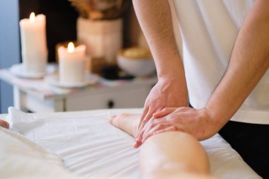 İnsan baldır kaslarına masaj yapan eller. Kadın bacağına baskı yapan terapist. Masaj terapistinin elleri masaj salonundaki genç bayanın bacaklarına masaj yapıyor. Genç bir kadın için kaplıca salonunda vücut bakımı.