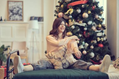 Genç bir kadın bir Noel ağacının arka planında bir yatakta oturuyor. Kutlamalardan sonra hayata yeniden başlama kavramı.