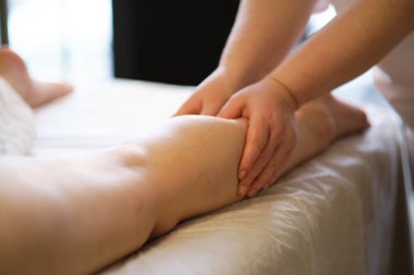 İnsan baldır kaslarına masaj yapan eller. Kadın bacağına baskı yapan terapist. Masaj terapistinin elleri masaj salonundaki genç bayanın bacaklarına masaj yapıyor. Genç bir kadın için kaplıca salonunda vücut bakımı.
