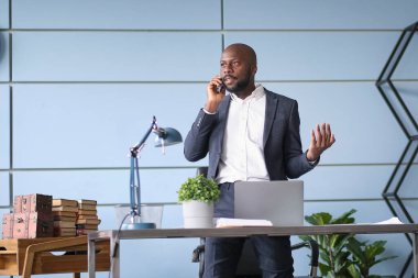 Sinirli Afrikalı Amerikalı iş adamı telefonda konuşuyor. Stresli patron, cep telefonuyla tartışıyor. Ofis masasında oturuyor.