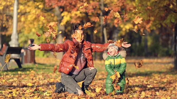 Mom and son throw autumn leaves in autumn park, family fun. family enjoying a walk in nature. happy motherhood concept. — Stock Photo, Image