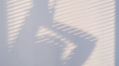 Panjurlar ve kadın silueti ile kapatılmış bir pencerenin gölgesi duvarda. Bulanık karanlık gölgeler duvarda hareket ediyor..