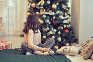 Genç bir kadın bir Noel ağacının arka planında bir yatakta oturuyor. Kutlamalardan sonra hayata yeniden başlama kavramı.