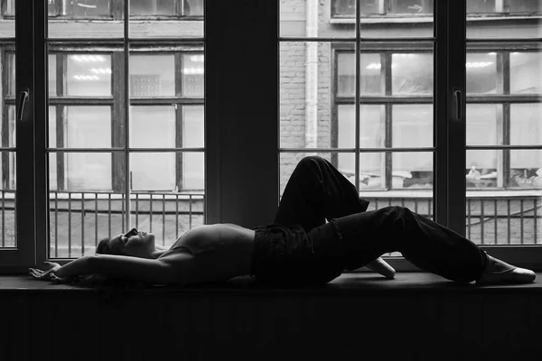 Foto en blanco y negro de la bailarina en el marco de la ventana en un edificio antiguo. Bailarina de ballet joven, elegante y elegante — Foto de Stock