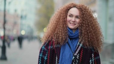 Güzel genç bir kadın kameraya bakıyor ve neşeyle gülümsüyor. Gün ışığında sokakta gülen surat. Dışarda olumlu bir portre.